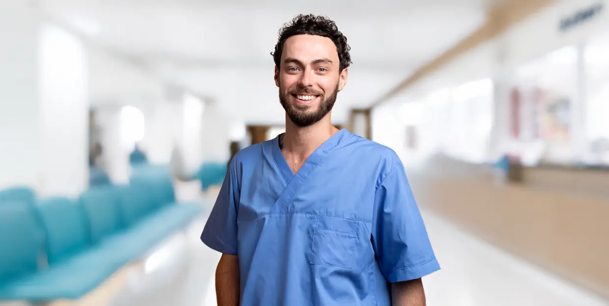 Corso Oss Sardegna - Cagliari 2025 -Uomo sorridente con divisa sanitaria azzurra, ha capelli corti scuri e ricci e la barba scura curata