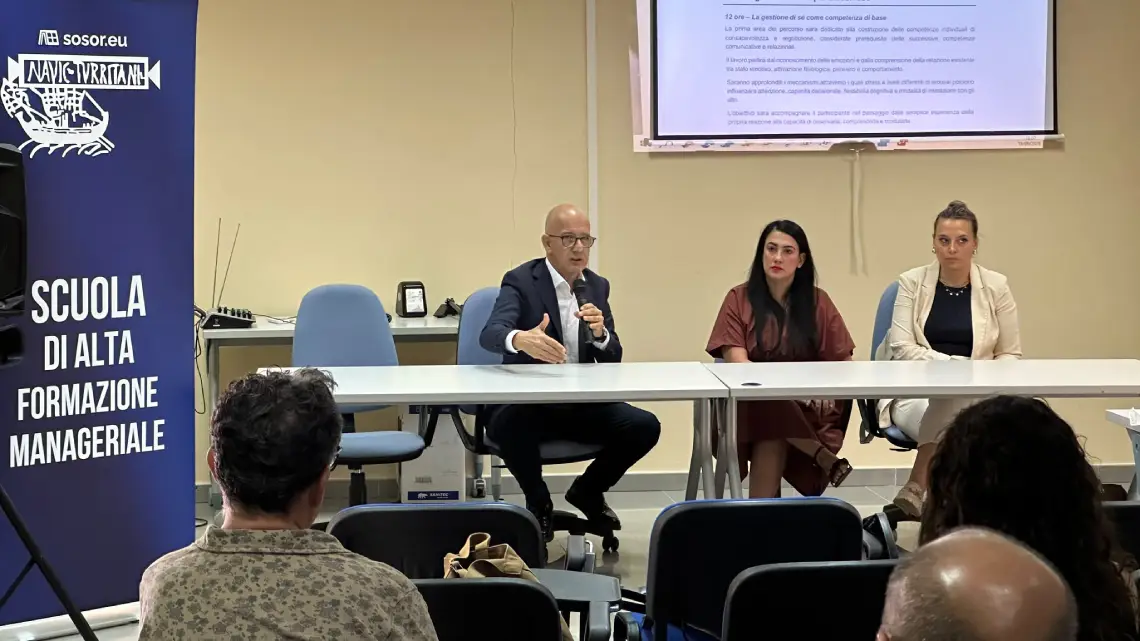 Pubblico in una sala conferenze assiste a inaugurazione Scuola Alta Formazione CIPSS. Un cartello sulla sinistra riporta la scritta "Sosor CIPSS, Scuola di alta formazione manageriale". Al tavolo dei relatori, Franco Sabatini parla al microfono. Accanto a lui presidente del CIPSS Simona Fois e Dalila Masia, docente del corso Negoziazione efficace