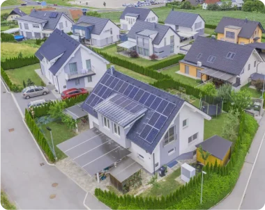 Veduta rappresentativa del progetto CER Sardegna. Un gruppo di case bianche viste dall'alto, circondate da prati. Il tetto della casa al centro è coperto da pannelli fotovoltaici.